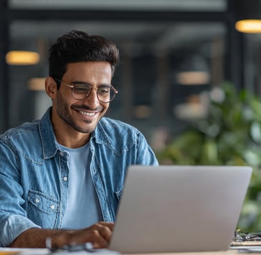 Smiling young male professional in glasses working on a laptop in a modern office.