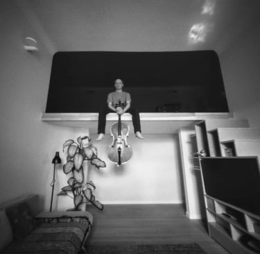 A man sitting on a bed in a room, holding cello