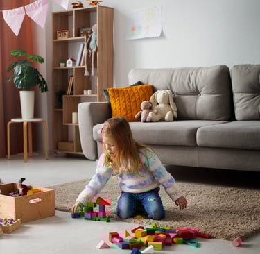 A young girl playing with blocks on the floor and a few toys decorated in background