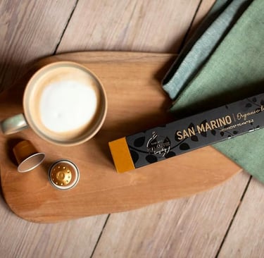 San Morino Real Coffee pods next to a latte on rustic table