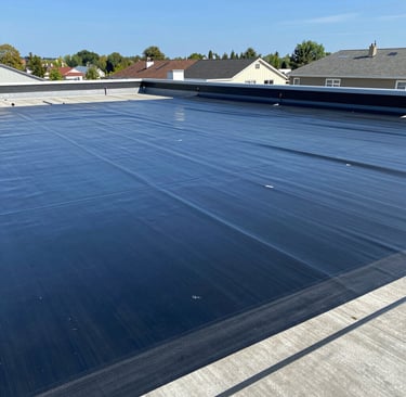 A person wearing safety gear is suspended by ropes, performing maintenance or cleaning on the side of a large building with vertical panels.