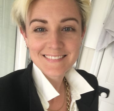 smiling blonde woman, blue eyes, dark eyebrows, wearing a white shirt, black jacket and gold chain