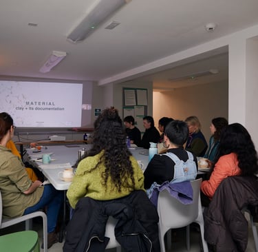 mixed group of people sitting round a table looking at a slide show, with backs to the camera