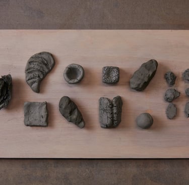 Various sculpted gray clay shapes on a wooden board. The clay was foraged from Devon, UK