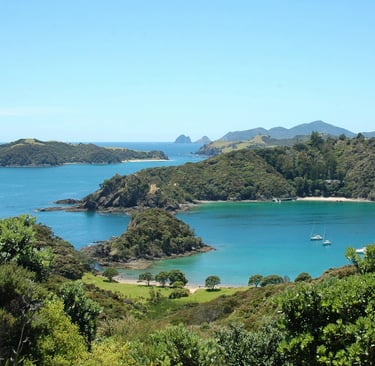 Aerial view of tropical islands and blue water in the Bay of Islands, New Zealand, with boats and lush greenery.