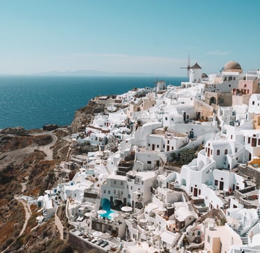 Panoramic view of white houses and a windmill on the cliffs of Oia, Santorini, overlooking the blue Aegean Sea.