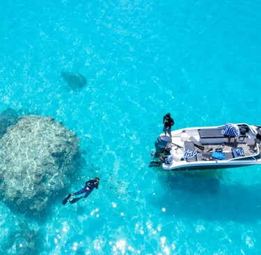 Aerial view of a boat and snorkeler in crystal clear turquoise tropical water near a coral reef.