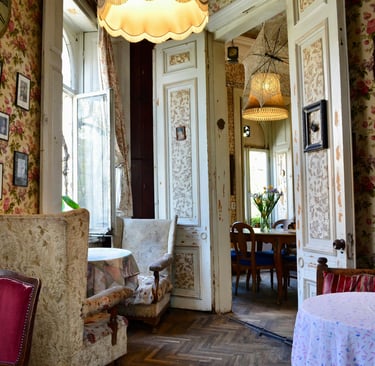 Vintage tea room with floral wallpaper, antique wingback chairs, and cozy tables in a classic European cafe.
