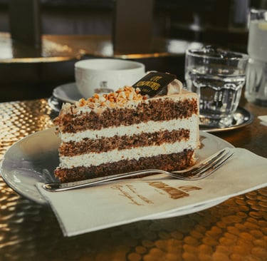 A slice of layered hazelnut cream cake topped with crushed nuts at a cafe.