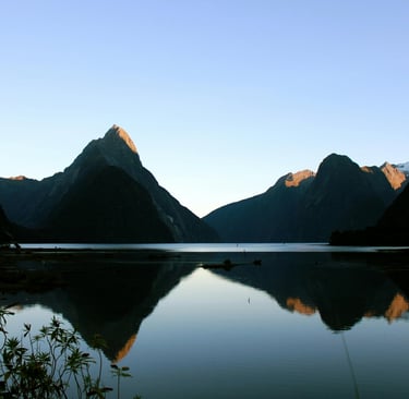 Milford Sound mountains reflected in calm water at sunrise in Fiordland National Park, New Zealand.