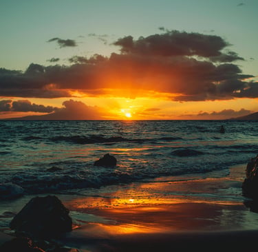 Golden tropical sunset over a dark sandy beach with ocean waves and dramatic clouds.