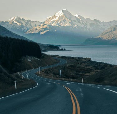 Winding mountain road leading toward snow-capped Mount Cook and Lake Pukaki in New Zealand.