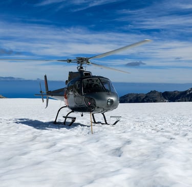 A grey scenic tour helicopter landed on a snowy mountain glacier under a blue sky.