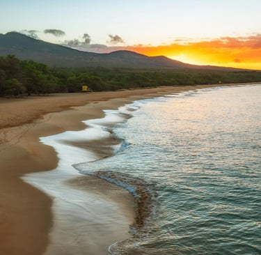 Golden sunset over Makena Beach in Maui with ocean waves washing onto the sandy tropical shoreline.
