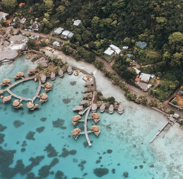 Aerial view of a tropical resort featuring overwater bungalows on clear turquoise water.