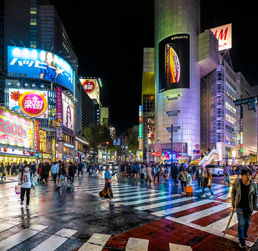 Shibuya Crossing Tokyo at night with illuminated buildings and crowds crossing intersection.