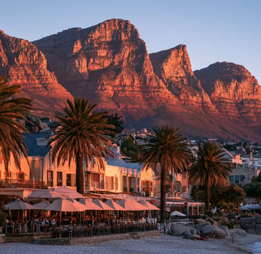 Camps Bay beach restaurants and palm trees at sunset with the Twelve Apostles mountains in Cape Town.