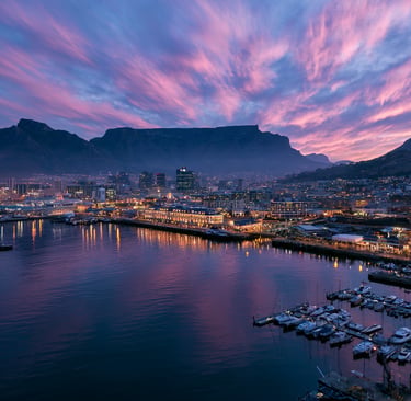 Cape Town V&A Waterfront and harbor at sunset with Table Mountain under a pink sky.