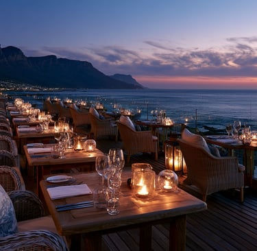 Luxury seaside restaurant at sunset with candlelit tables overlooking the ocean and mountains.