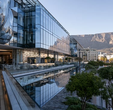 Modern glass architecture at the V&A Waterfront in Cape Town with Table Mountain in the background.