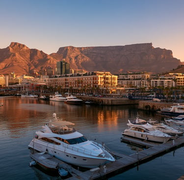Luxury yachts moored at V&A Waterfront harbor with Table Mountain at sunset in Cape Town, South Africa.