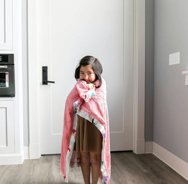 a little girl standing in a room with a pink blanket