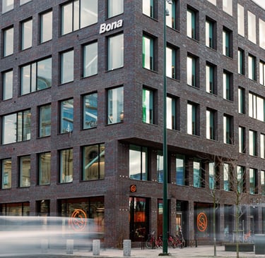 Modern dark brick Bona office building with large windows on a city street corner.