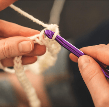 une personne crochète un morceau de laine avec une paire de mains