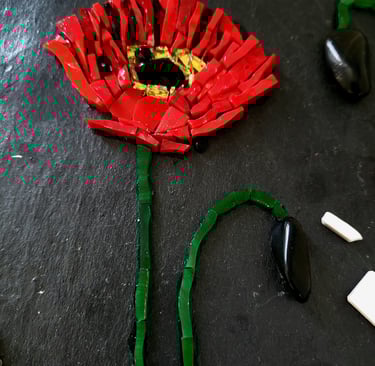 a red flower with a green ribbon on it. Un coquelicot en mosaique. Début de création