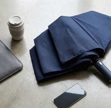 Flat lay payung lipat stylish dan perlengkapan kerja esensial.