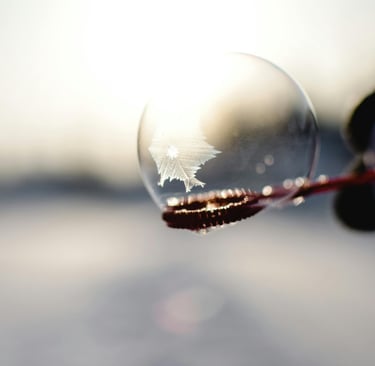 a person holding a soap bubble in front of a sun with a snowflake crystal forming