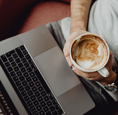 an image of man with a laptop on his lap sitting on a couch holding a cup of coffee in a coffee shop