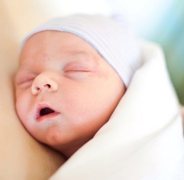 A peaceful newborn baby sleeping in a hospital swaddle blanket and blue striped beanie.