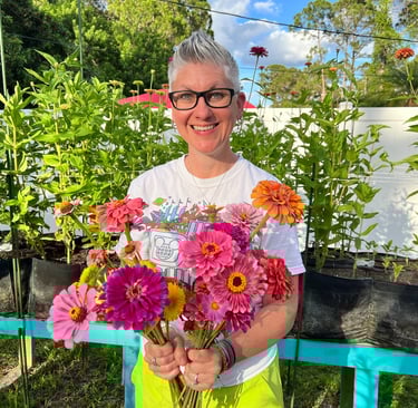 Steph holding zinnias standing in front of a raised cut flower bed