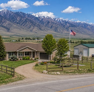 A scenic mountain ranch home with a large detached workshop, fenced yard, and American flag.