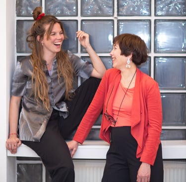 Two smiling female public speaking trainers in Berlin, looking at each other