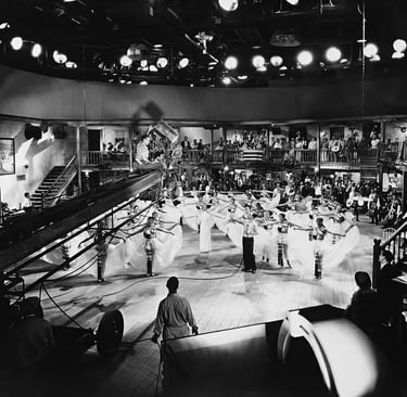 Berkeley perched on a crane with camera crew filming dancers holding skirts in symmetrical patterns.