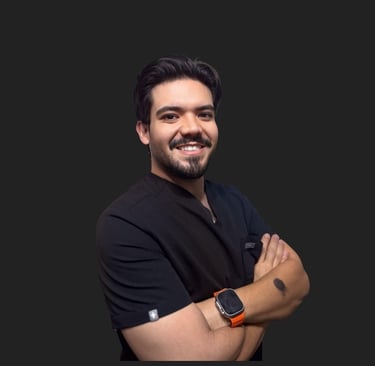 Smiling male healthcare professional in black scrubs with arms crossed against a dark background.
