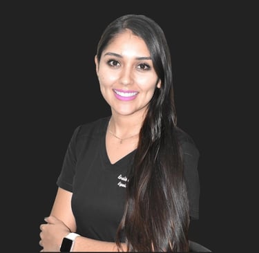 Smiling female medical professional with long dark hair wearing black scrubs against a dark background.