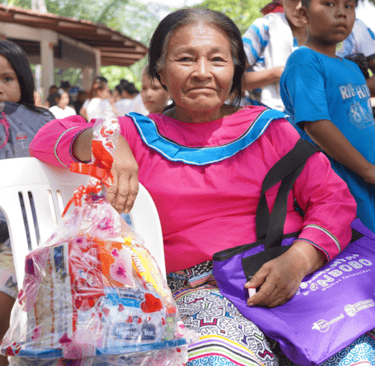 An indigenous woman in a pink blouse holding a gift basket at an event organized by Roger Bardales.