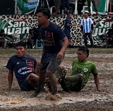 Athletes competing in a muddy soccer match on a rain-soaked field during a local tournament.