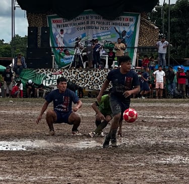 Athletes playing soccer on a muddy field during the Copa Indigena 2025 indigenous people's football tournament.