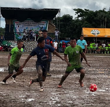 Muddy soccer players competing for the ball during an indigenous community tournament match.