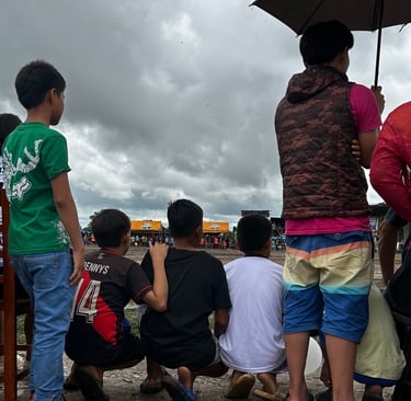 Young boys watching a local outdoor community event under a cloudy sky.