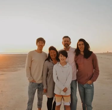 interracial caucasian and asian family with 2 teenage boys and 1 preteen boy at sunset smiling on the beach