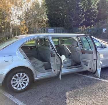 Silver stretch limousine parked in a lot with all four side doors open, revealing a light-colored leather interior.