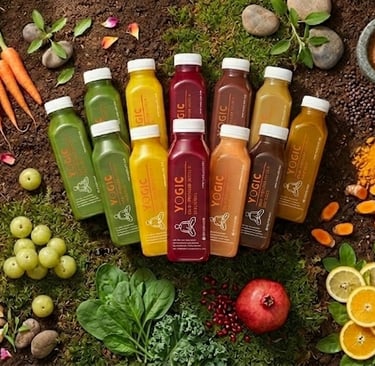 Yogic cold-pressed juices surrounded by fresh fruits, vegetables, and herbal powders on soil.