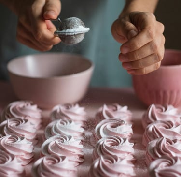 Un panadero espolvoreando panqueques en espiral rosa con azúcar glas usando un colador.