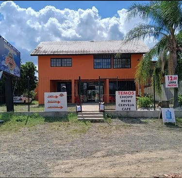 Entrada da loja de conveniência DUGIBA. Prédio laranja com placas de sinalização de produtos e servi