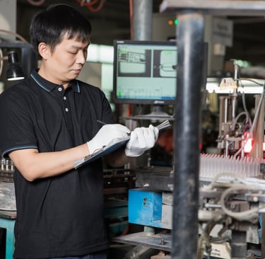 A factory quality control technician in white gloves inspecting a production line with a clipboard.